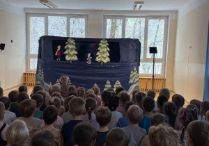 Dzieci siedzą na ławeczkach i oglądają teatrzyk kukiełkowy