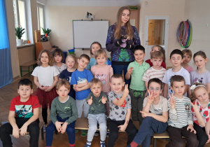 Dzieci siedzą na ławeczkach wspólnie z panią trzymającą w ręku fretkę