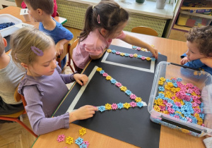 Dziewczynki układają z klocków rytmy do szablonu na kartonie