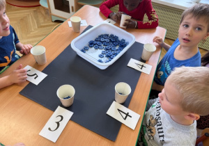 Chłopcy wkładają do kubeczki tyle klocków, ile wskazuje liczba