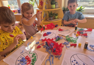 Dzieci przyklejają kuleczki z bibuły na karton