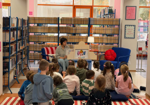 Dzieci siedza na dywanie i słuchają opowiadania bibliotekarki