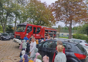 Dzieci stoją przed budynkiem przedszkola i oglądają wóz strażacki