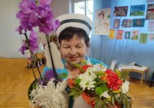 Pani Bożenka w stroju pielęgniarki trzyma kwiaty od dzieci z okazji Dnia Pielęgniarki.